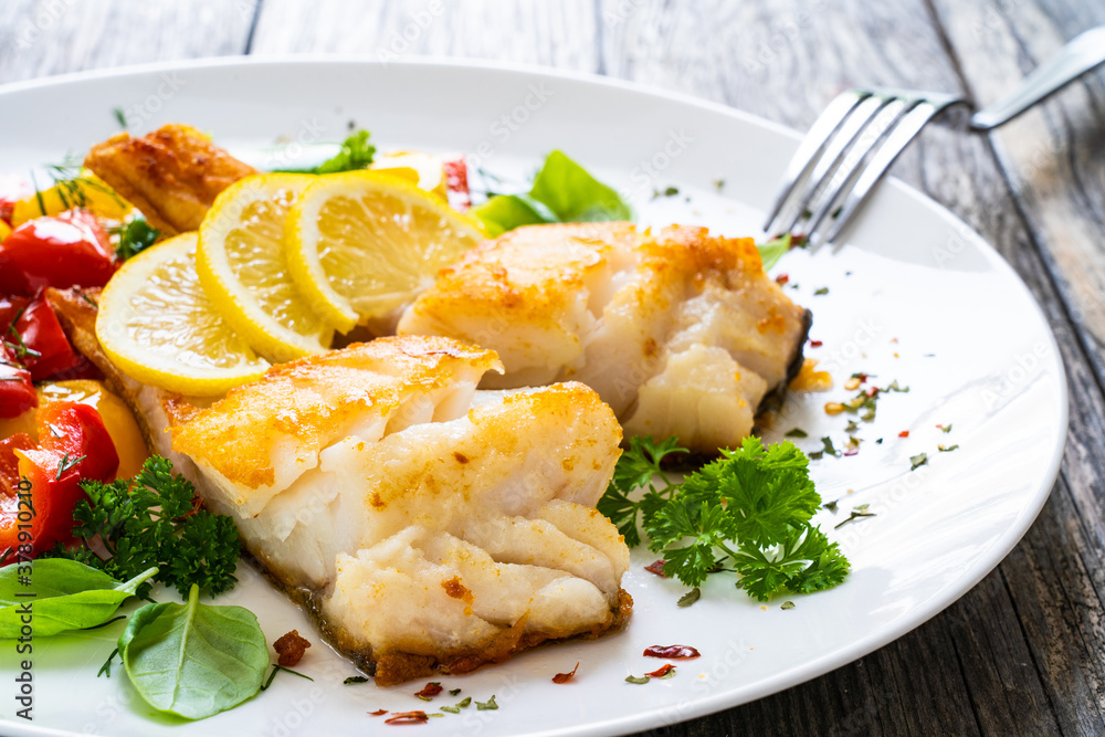 Fish dish - fried cod fillet with fried vegetables and lemon served on wooden table Fish dish - fried cod fillet with fried vegetables and lemon served on wooden table