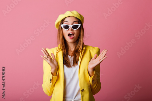 Close up fashion portrait of cute stylish girl in yellow suit and beret. Trendy glasses, pastel colors. Pink background.