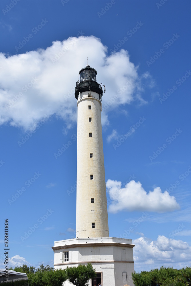 Tall white lighthouse over a blue sky sorrunded by some clouds