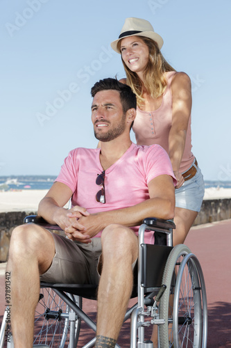 woman pushing attractive man in wheelchair along beach promenade © auremar