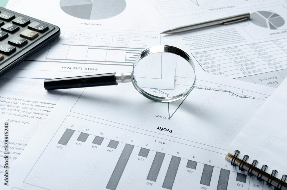 Magnifying glass, pen, calculator, notebook and business documnts, graphs and charts of profit and sales information.Profit jump Magnifying glass, pen, calculator, notebook and business documnts, graphs and charts of profit and sales information.Profit jump