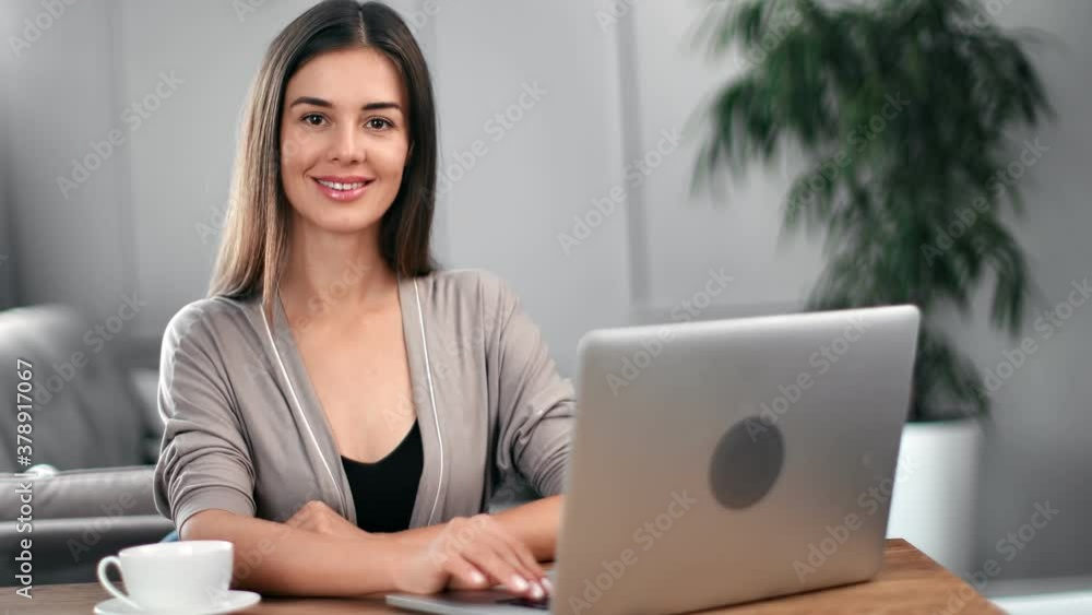 Portrait of pretty modern woman posing sitting at desk in home or office. Medium shot on RED camera Portrait of pretty modern woman posing sitting at desk in home or office. Medium shot on RED camera