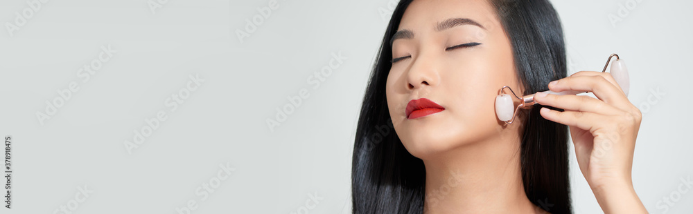 Face massage. Smiling woman using rose quartz facial roller for skin care, beauty treatment on white isolate background. Face massage. Smiling woman using rose quartz facial roller for skin care, beauty treatment on white isolate background.