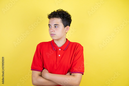 Beautiful teenager boy over isolated yellow background skeptic and nervous, disapproving expression on face with arms crossed