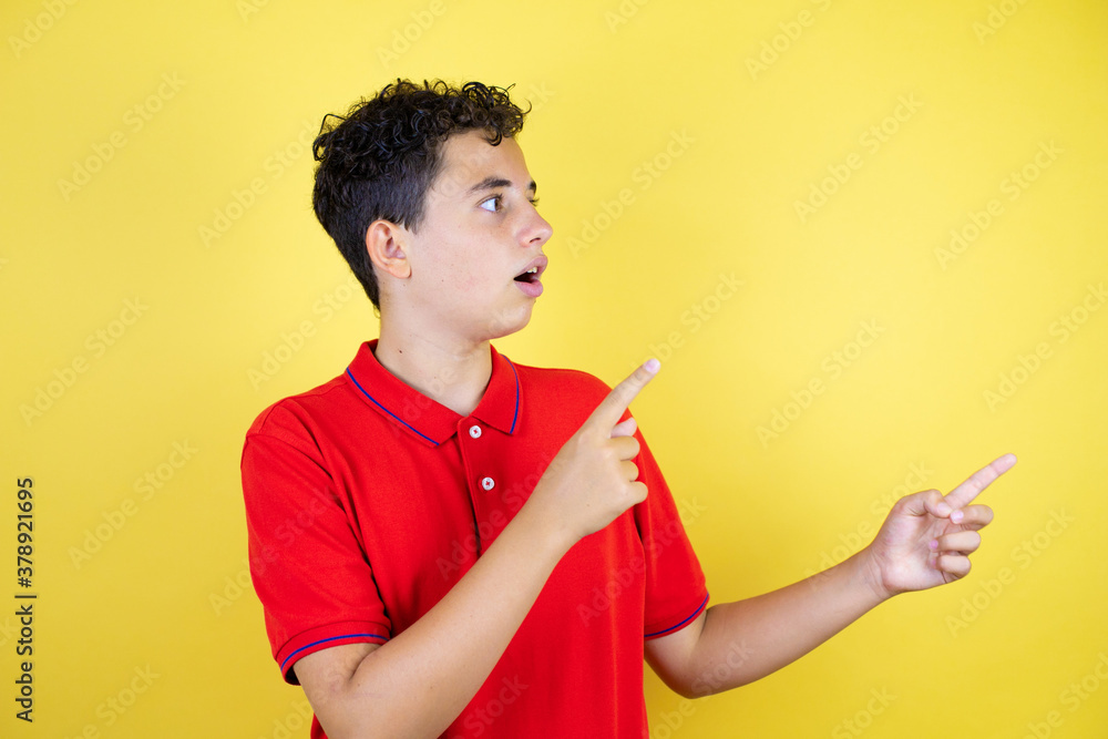 Beautiful teenager boy over isolated yellow background surprised, looking and pointing side Beautiful teenager boy over isolated yellow background surprised, looking and pointing side