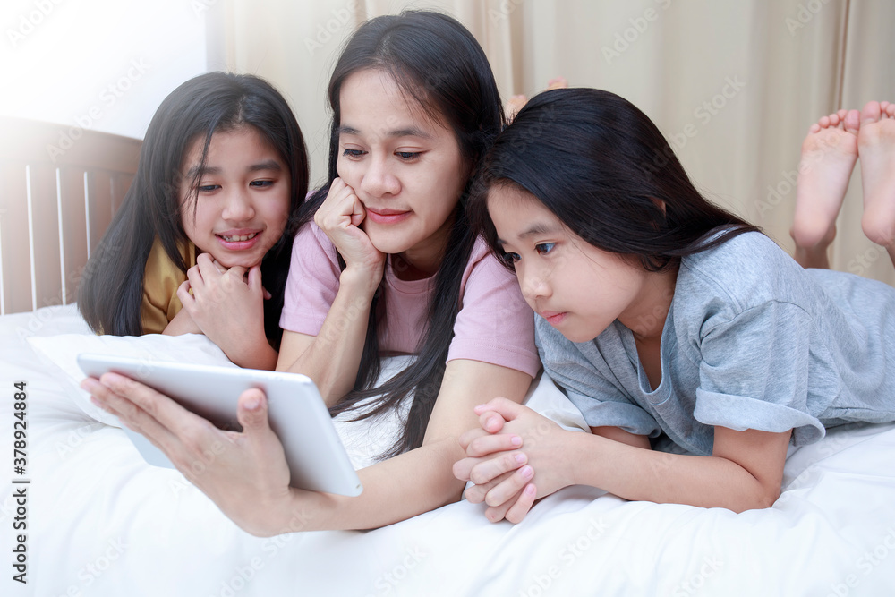 Happy Asian family enjoy and relax on bed in bedroom. mother and daughters enjoy using tablet together on bed. Family concept. Happy Asian family enjoy and relax on bed in bedroom. mother and daughters enjoy using tablet together on bed. Family concept.