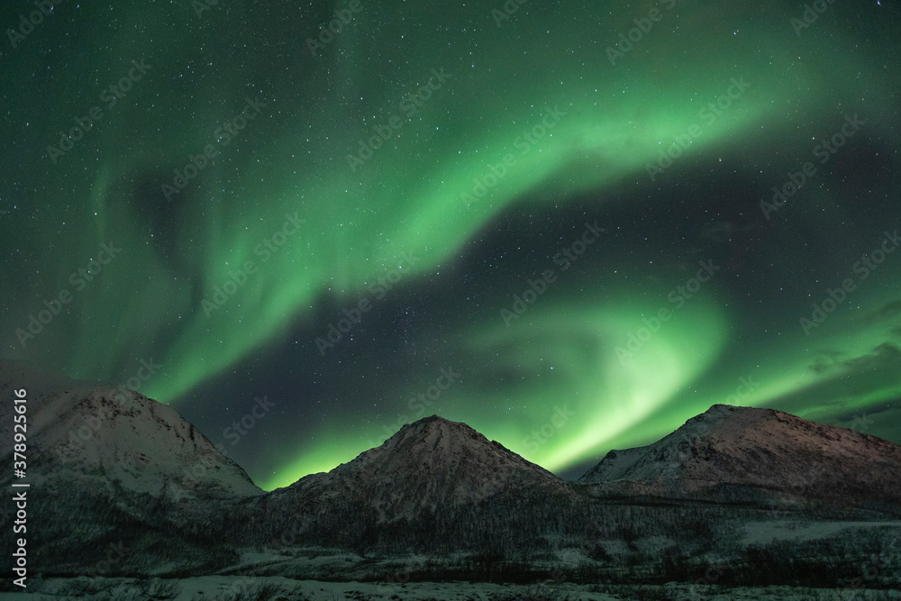 Night sky full of northern lights (auroras) over stunning mountains peaks in Norway 