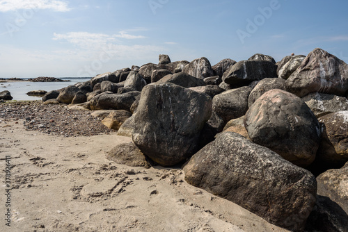 Runde Felsen als Buhnen im Sand vor aufgelockertem Himmel