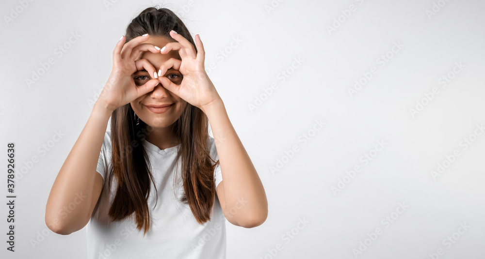 Cheerful girl in casual light clothes holding hands near eyes, imitating glasses or binoculars. Copy space Cheerful girl in casual light clothes holding hands near eyes, imitating glasses or binoculars. Copy space