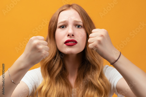 Pretty girl with wavy redhead, raising fists frustrated and furious