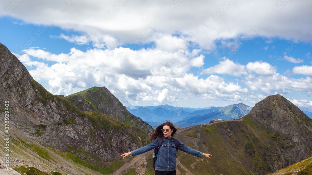 A young female tourist on top of a mountain on the panorama background.