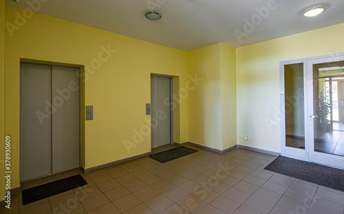 Modern interior of entrance in living complex. Elevators. Tile floor. Yellow walls.