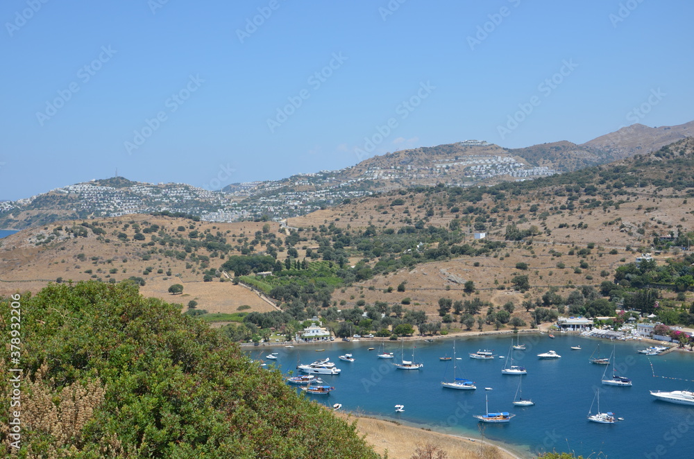 Top view of an entire bay of the Aegean Sea. Sailboats and boats moored. Settlements spread over the hills.