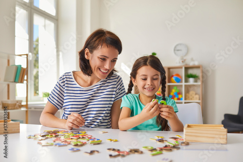 Mom and little daughter put together puzzles while sitting at a table in the room.