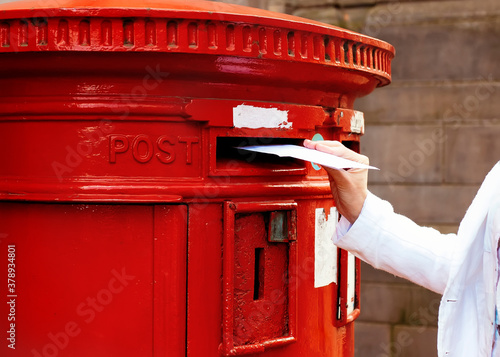 Murais de parede woman putting a card to red postbox and walking around English city