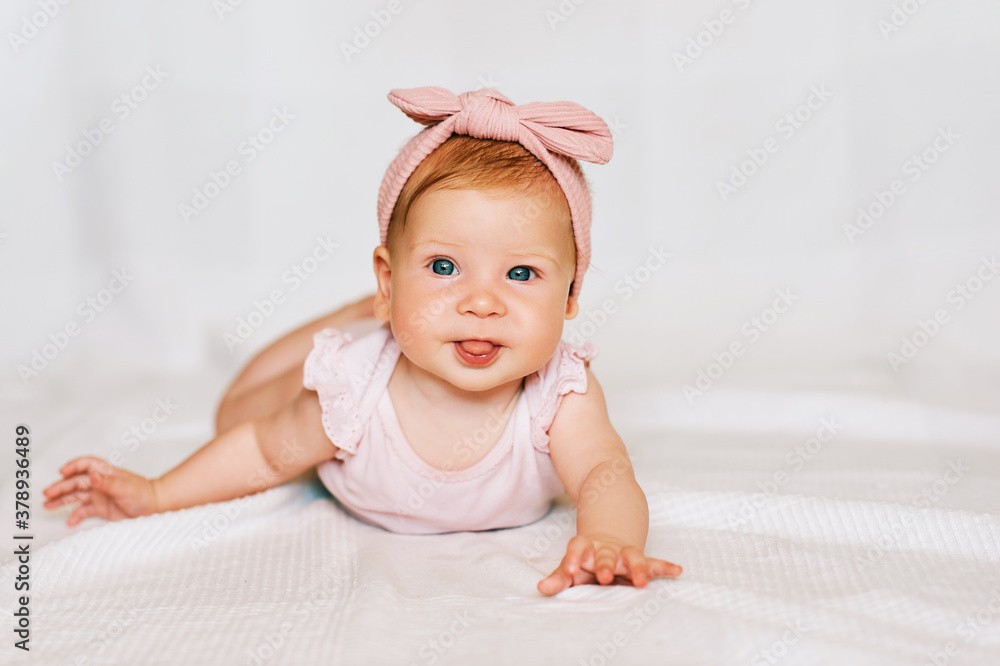 Portrait of adorable red-haired baby lying on belly, white background, wearing pink body and headband, looking straight to camera Portrait of adorable red-haired baby lying on belly, white background, wearing pink body and headband, looking straight to camera