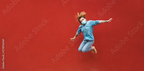 Tattoo girl jumping outdoor wearing safety mask with red wall in background