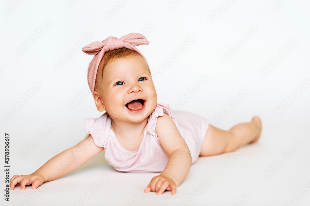 Portrait of adorable red-haired baby lying on belly, white background, wearing pink body and headband Portrait of adorable red-haired baby lying on belly, white background, wearing pink body and headband