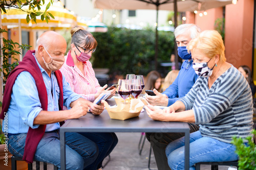 Retired  friends with face mask watching smartphone while drinking red wine at restaurant photo