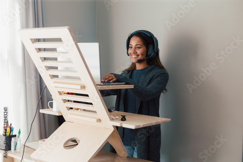 Young woman working on laptop at standing desk with earphones