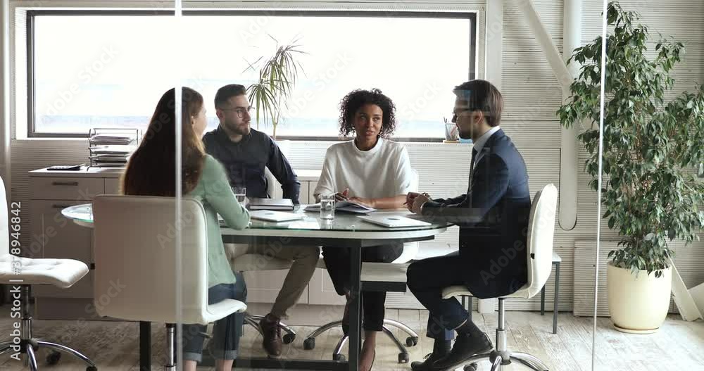 Full length confident young boss team leader in suit holding brainstorming meeting with diverse mixed race colleagues in office. Happy multiracial employees discussing project details at workplace. Full length confident young boss team leader in suit holding brainstorming meeting with diverse mixed race colleagues in office. Happy multiracial employees discussing project details at workplace.