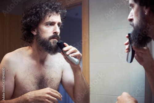 Middle-aged hispanic man cutting his beard