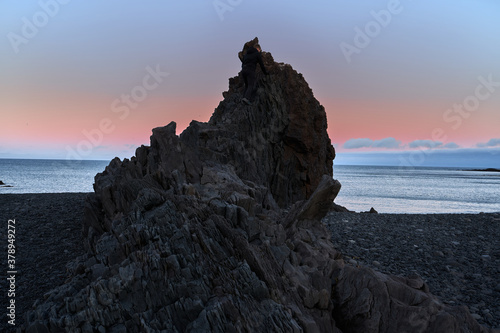 Iconic and beautiful sunrise at Djupalonssandur beach with its mound of rocks eroded by sea water and a man climbing them with his camera on the island of Iceland