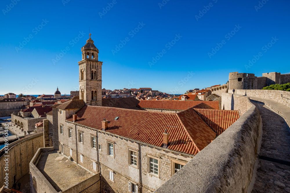 Colorful fortress street walk scene, clear sky sunny day. Church bell tower, building roofs. Winter view of Mediterranean old city Dubrovnik, famous European travel and historic destination, Croatia