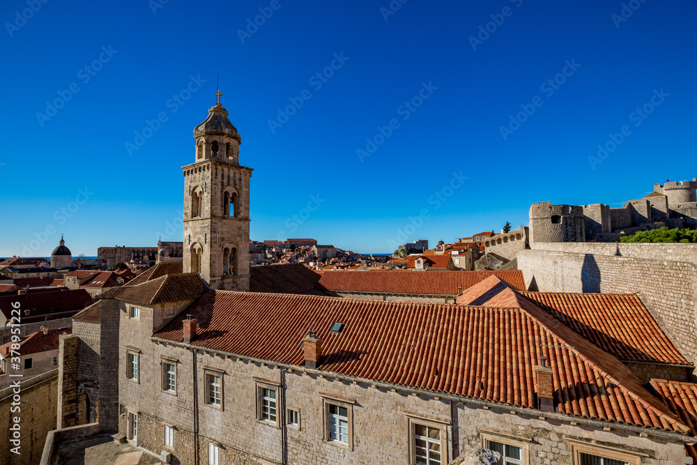 Colorful fortress street walk scene, clear sky sunny day. Church bell tower, building roofs. Winter view of Mediterranean old city Dubrovnik, famous European travel and historic destination, Croatia