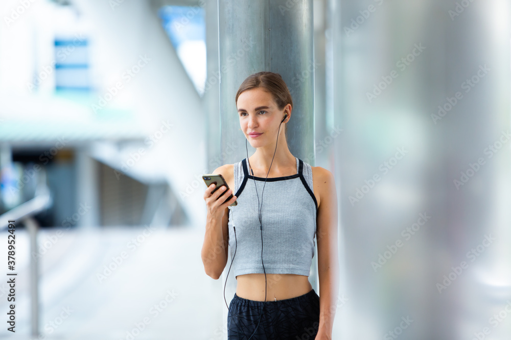 Portrait of fit and sporty young woman asian outdoors listening music using mobile phone.  Fitness female looking relaxed in city