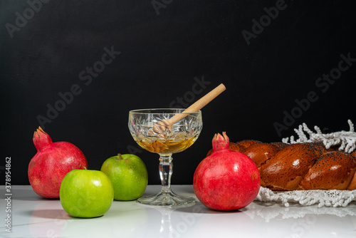 Apples, pomegranates, honey and wicker challah on a wooden table.