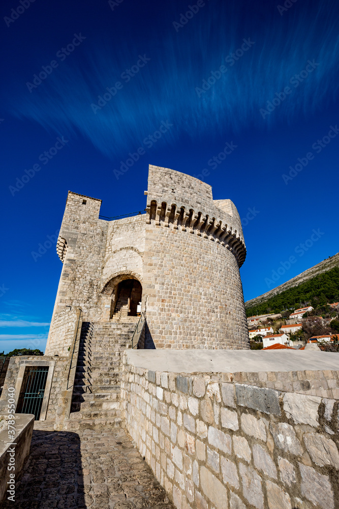 Colorful fortress street walk scene, clear sky sunny day. Tower low angle view. Scenery winter view of Mediterranean old city of Dubrovnik, famous European travel and historic destination, Croatia