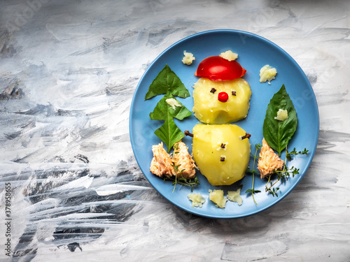 Christmas breakfast for the child. Snowman made of potatoes and green Christmas trees from basil on a blue plate © Elena