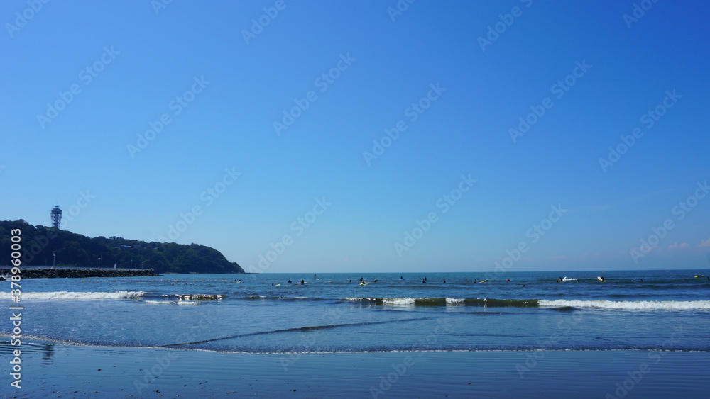 People surfing on sea waves under blue sky. Katase Nishihama beach is one of Japan's most popular beaches. Beach next to Enoshima Island