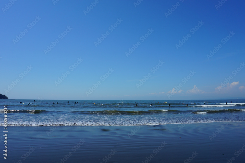 People surfing on sea waves under blue sky. Katase Nishihama beach is one of Japan's most popular beaches
