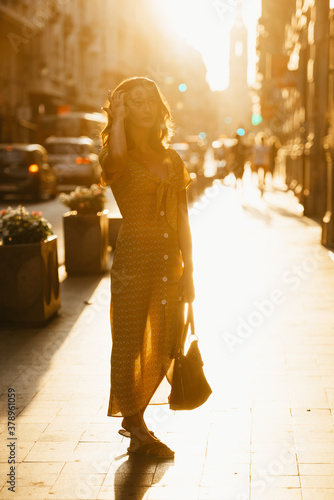 A woman in a dress with a plunging neckline holds a bag on the sunset in Spain.