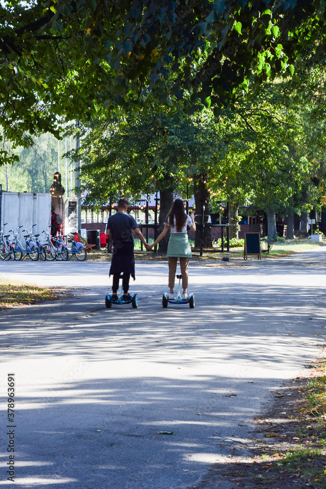 A guy and a girl ride a hoverboard with their backs in the park and hold hands