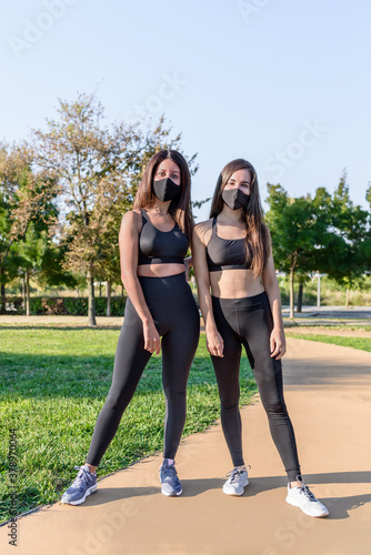 two women wearing sport clothing and black face mask posing for picture in green park