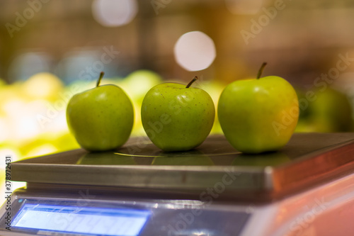Fototapeta Naklejka Na Ścianę i Meble -  Closeup of three apples lying on weight scale.  Blurred background. Selective focus.