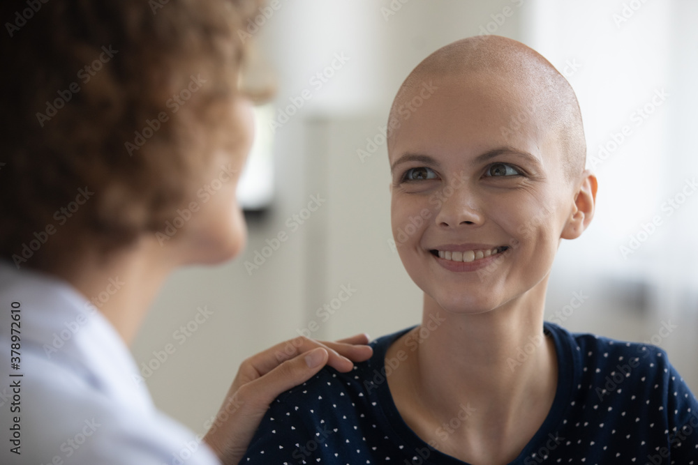 Fototapeta premium Close up of smiling young Caucasian sick hairless woman talk with doctor at consultation in hospital. Nurse comfort support happy ill bald female cancer patient. Oncology, healthcare concept.