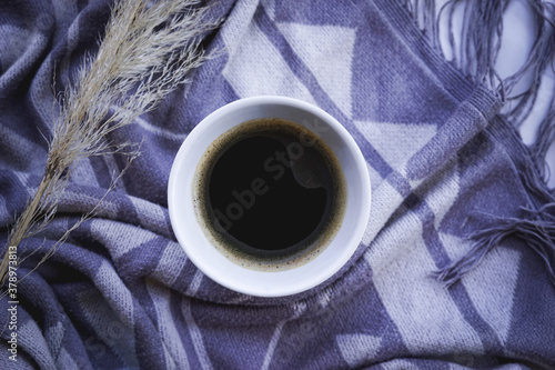 Cup of black coffee on blue / grey & white print blanket. Composition with reed. Cozy and relaxing still life photography.