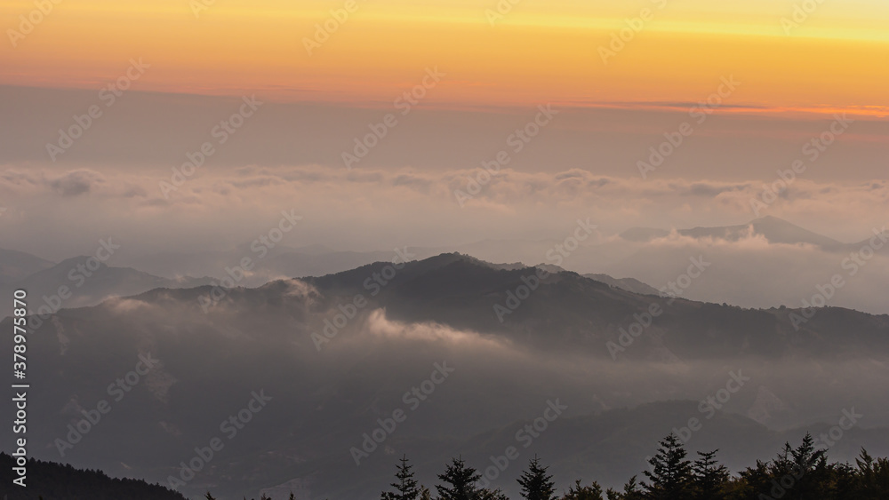 Zdjęcie przedstawia nadchodzący wschód słońca przeplatający się z piękną warstwą chmur widoczną ponad szczytami gór.