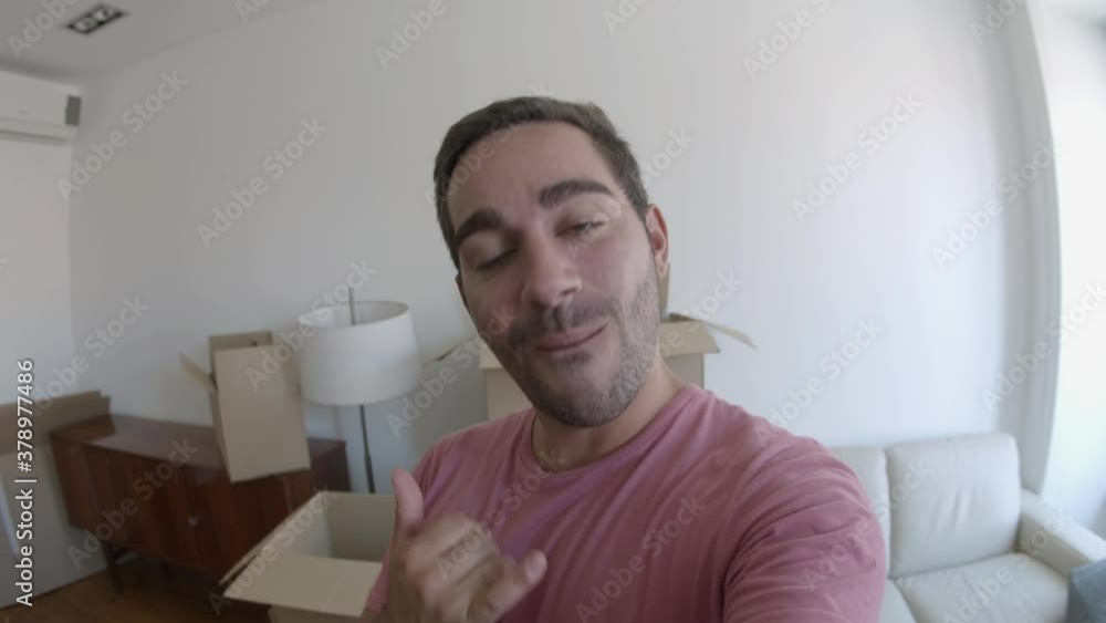 Cheerful attractive man video chatting, smiling and showing new apartment during conference. Young Caucasian guy in pink shirt talking about moving in new house. Relocation and accommodation concept Cheerful attractive man video chatting, smiling and showing new apartment during conference. Young Caucasian guy in pink shirt talking about moving in new house. Relocation and accommodation concept