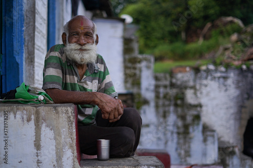 An old indian man with long and white beard sitting on the stairs wearing rugged clothes. photo