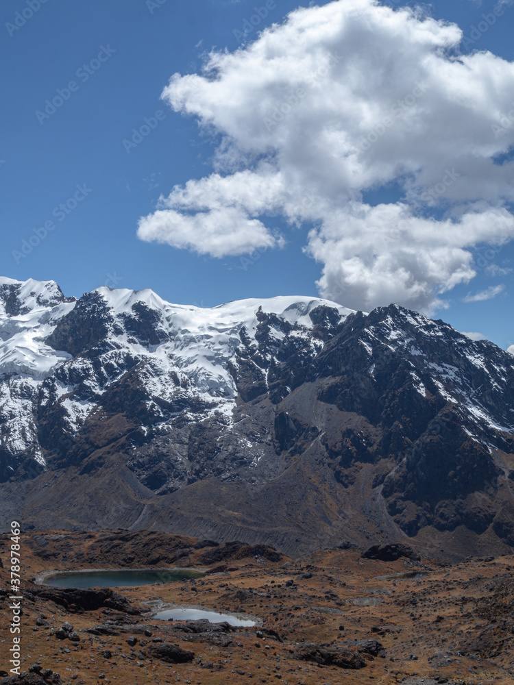 Vertical landscape of huge mountains with snow and ice and a blue lake with blue sky and clouds, in Huancayo, peru
