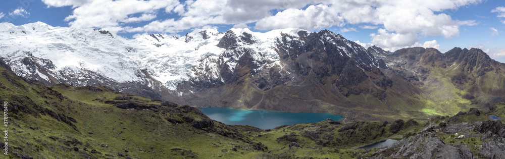 Fototapeta premium Panorama landscape of huge green mountains with snow and ice and a lake with blue sky and clouds, in cordilera Huaytapallana, Huancayo, peru