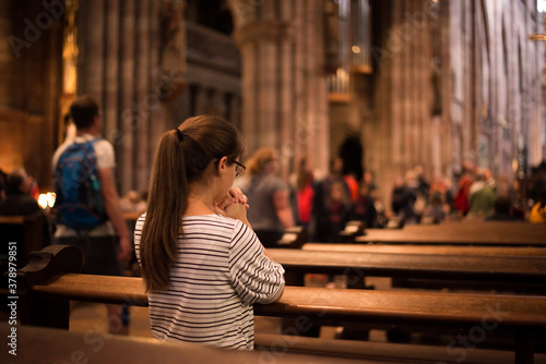 Girl in a church standing on her knees. Young religious woman in glasses with long dark hair, praying in catholic cathedral.