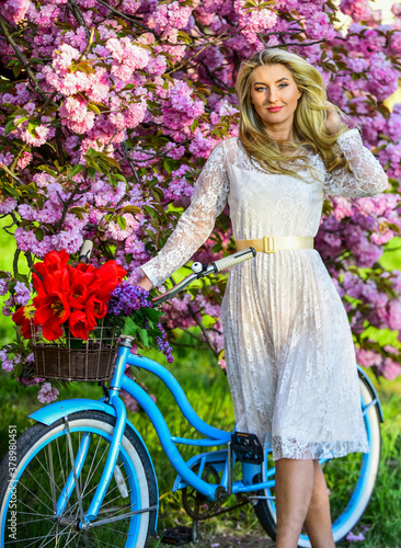girl carry flowers in retro bicycle. spring beautiful woman in dress. girl vintage bike. blooming sakura tree. summer fashion and beauty. lady walk in park. pink cherry tree blossom. Amazing summer
