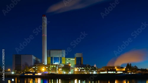 Evening timelapse sequence of a modern waste incineration plant in Oberhausen, Germany in the night in 4K, with a ship docking at the canal shore, zooming in.