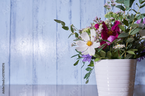  Close-up of multicolored wildflowers standing in a white vase against a blue wall     